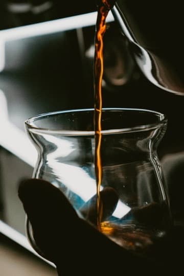 café cayendo en una taza de vidrio sostenida en la mano